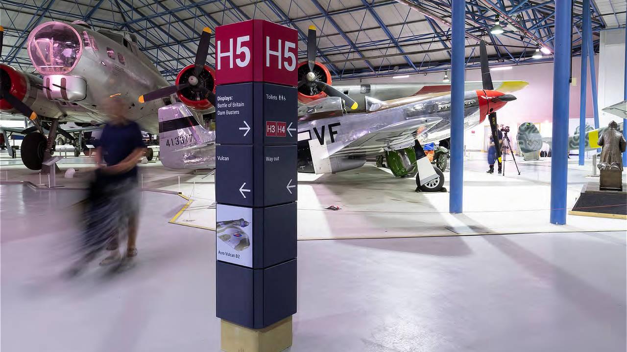 RAF Museum signage post in aircraft hangar, with vintage aeroplanes in the background